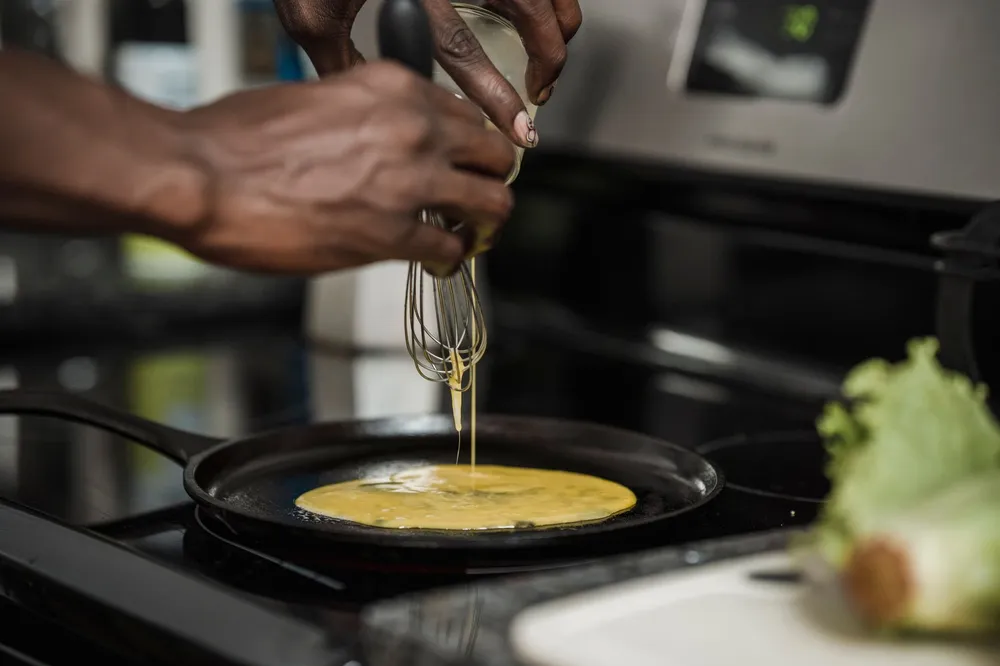 Pâte à crêpes versée dans une poêle plate posée sur le feu, filet de pâte qui coule du récipient