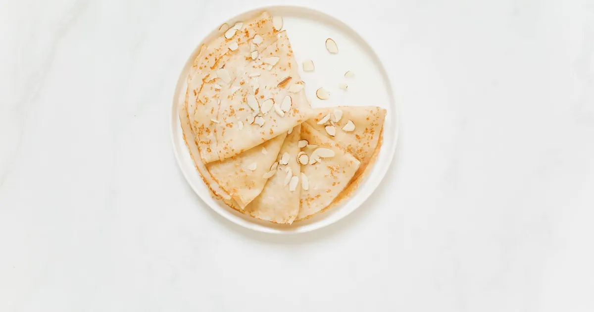 Pile de crêpes nature sans sucre sur une assiette, à côté d'une louche de pâte
