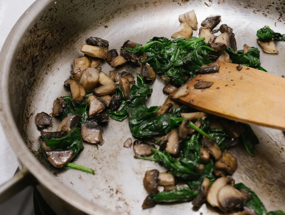 Champignons et épinards frais dans une poêle en inox, prêts à garnir une galette de sarrasin