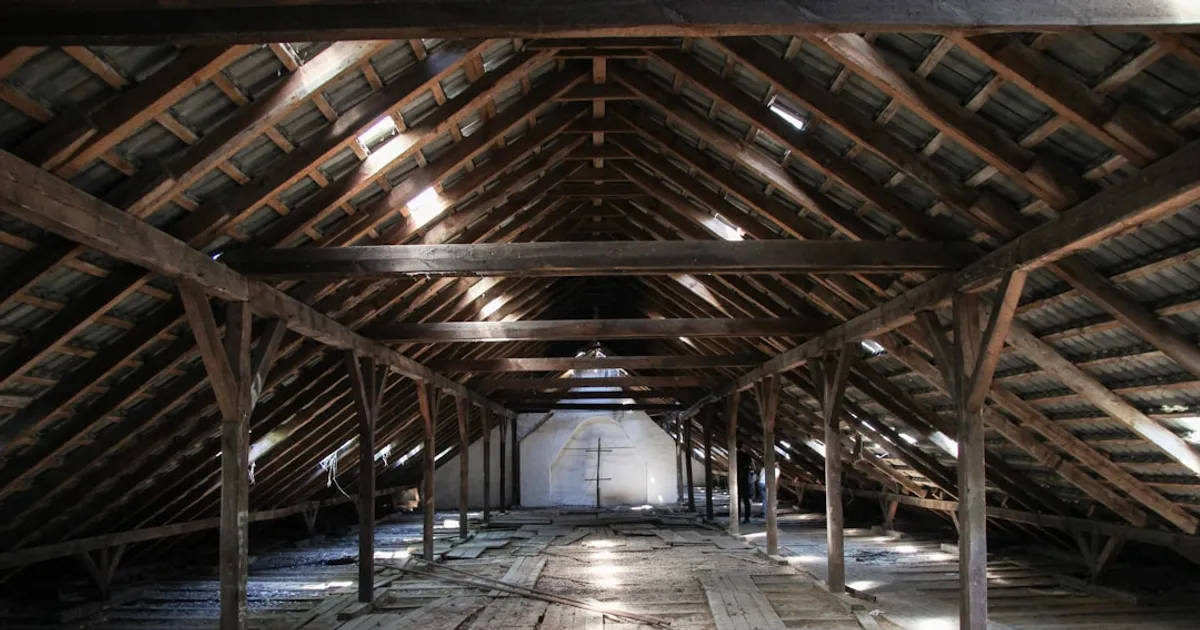 Grand grenier d'une vieille maison, charpente en bois apparente et plancher de planches, lumière du jour entre les tuiles